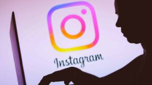 In this photo illustration, the Instagram logo is seen in the background of a silhouette of a person using a notebook.