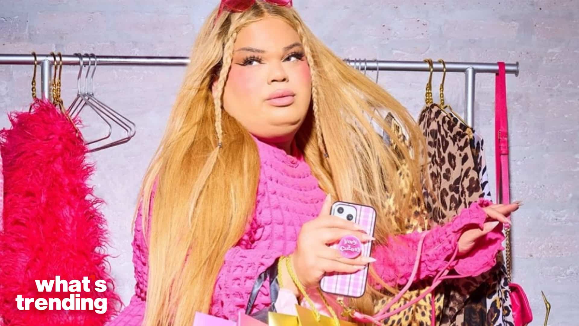 Person with long blonde hair in a pink textured top holding a phone with a pink plaid case and shopping bags