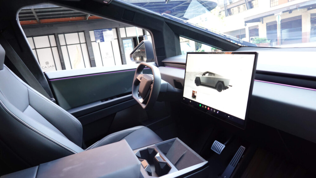 Tesla Cybertruck interior showing steering wheel, large touchscreen, and center console cup holders