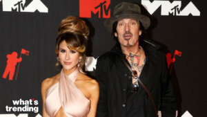 Couple posing on the MTV red carpet, woman in a pink halter dress and man with tattoos wearing a black shirt and hat