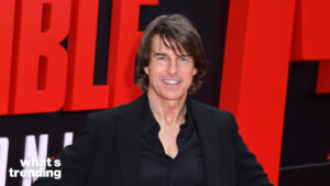Tom Cruise smiling at the Mission Impossible movie premiere with a red and black background