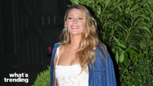 Blake Lively smiling in a white lace dress and blue jacket outdoors at night