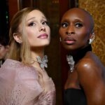 Two women dressed elegantly, one in a pink embellished gown with a butterfly necklace, the other in a black strapless dress with silver jewelry.