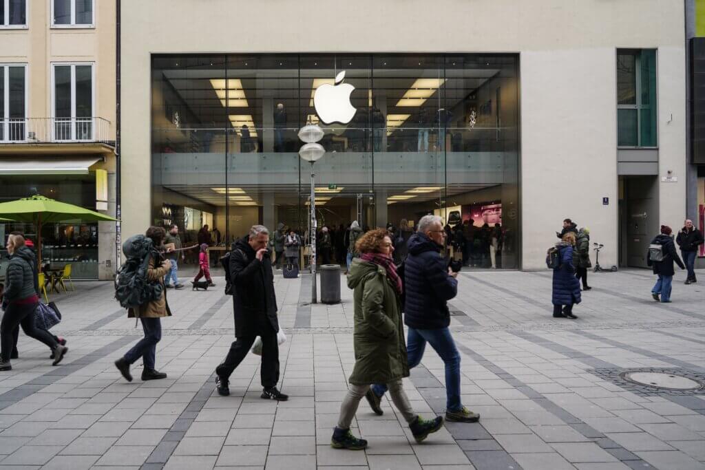 People walking in front of an Apple Store with a large illuminated Apple logo above the entrance.