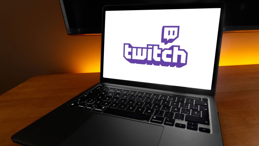 MacBook Pro laptop displaying the Twitch logo on screen on a wooden desk with orange backlight