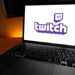 MacBook Pro laptop displaying the Twitch logo on screen on a wooden desk with orange backlight