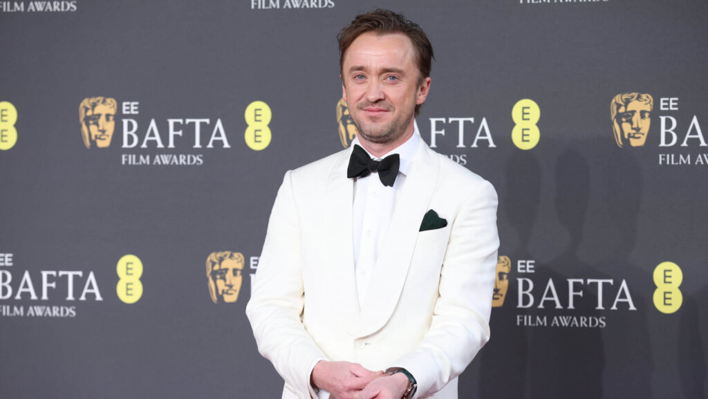 Tom Felton wearing a white tuxedo with black bow tie at the BAFTA Film Awards red carpet.