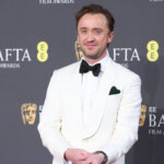 Tom Felton wearing a white tuxedo with black bow tie at the BAFTA Film Awards red carpet.