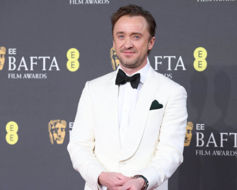 Tom Felton wearing a white tuxedo with black bow tie at the BAFTA Film Awards red carpet.