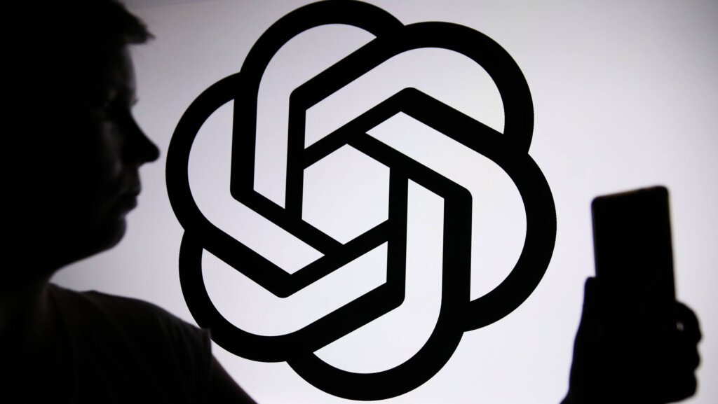 Silhouette of a person holding a phone in front of a large OpenAI logo on a white background.
