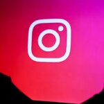 Silhouette of a person holding a smartphone in front of a screen displaying the Instagram logo on a red-pink gradient background