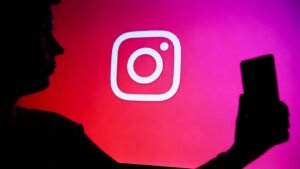 Silhouette of a person holding a smartphone in front of a screen displaying the Instagram logo on a red-pink gradient background