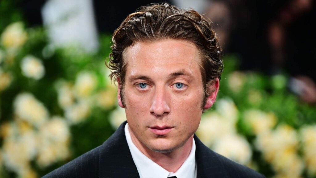 Actor Paul Dano with slicked-back hair wearing a black suit and white shirt at a formal event