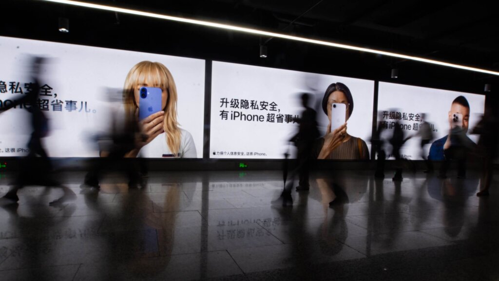 People walking past large illuminated Apple iPhone privacy feature advertisements in a subway station.