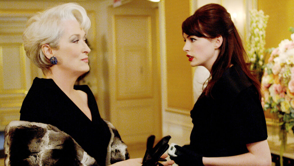 Meryl Streep and Anne Hathaway in a scene from The Devil Wears Prada, dressed in black with a fur coat and gloves.