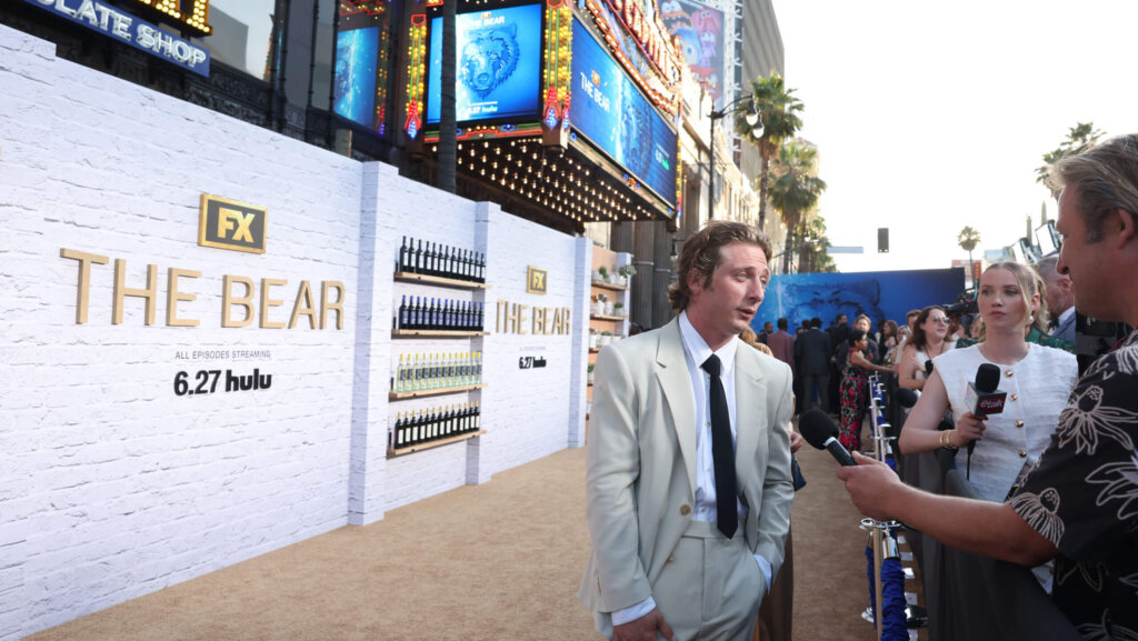 Actor Jeremy Allen White in a light suit being interviewed at FX The Bear premiere event on a beige carpet.