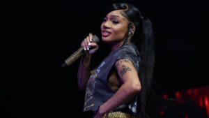 Rapper Megan Thee Stallion performing on stage holding a gold microphone with tattoos visible on her arms.