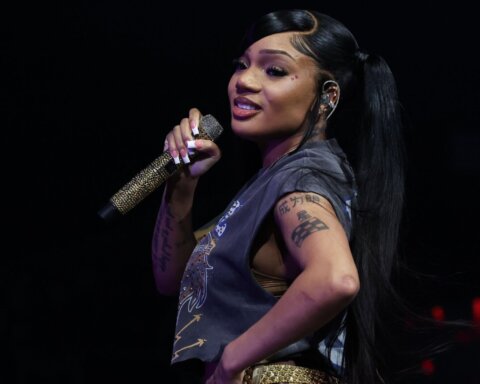 Rapper Megan Thee Stallion performing on stage holding a gold microphone with tattoos visible on her arms.