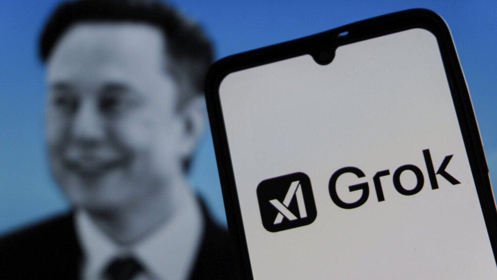 Smartphone displaying Grok logo with blurred image of Elon Musk in the background