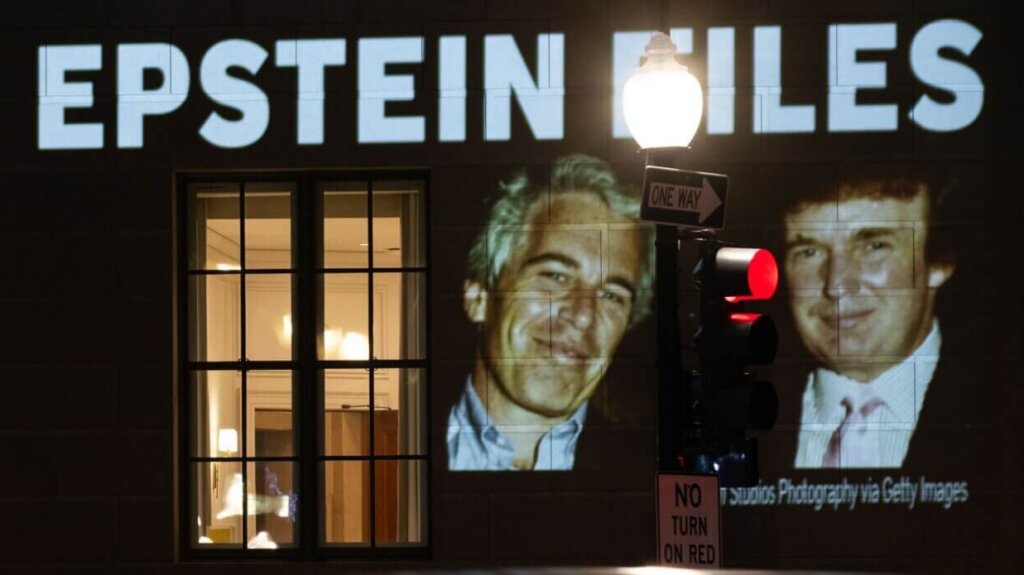 Projection on building reading "President Trump: Release all the Epstein files" with photos of Jeffrey Epstein and Donald Trump at night