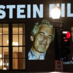 Projection on building reading "President Trump: Release all the Epstein files" with photos of Jeffrey Epstein and Donald Trump at night