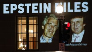 Projection on building reading "President Trump: Release all the Epstein files" with photos of Jeffrey Epstein and Donald Trump at night