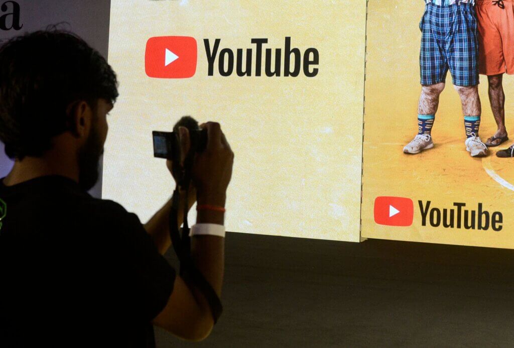 Person taking a photo of a screen displaying the YouTube logo and part of two people wearing shorts and sneakers