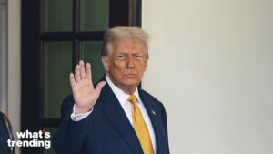 Donald Trump in a suit and yellow tie raising his hand in a waving gesture near a door with a "what's trending" logo.