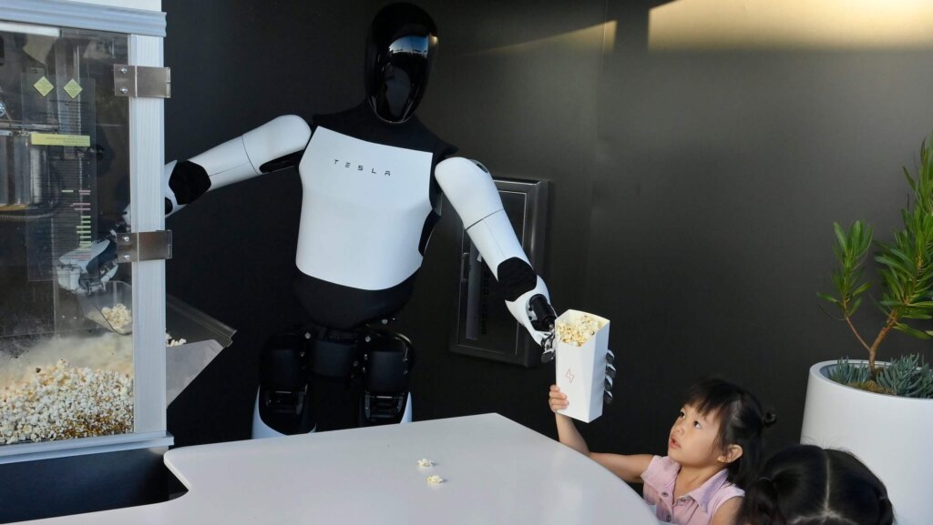 Tesla robot serving popcorn to a child at a counter with a popcorn machine in the background