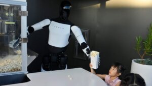 Tesla robot serving popcorn to a child at a counter with a popcorn machine in the background