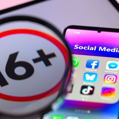 Magnified 16+ age restriction symbol next to smartphone showing social media apps Facebook, Messenger, Instagram, TikTok.