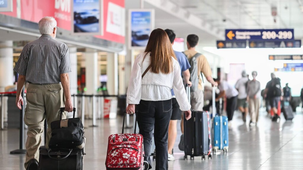 Travelers walking with rolling suitcases in an airport terminal near gate signs 200-299