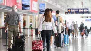 Travelers walking with rolling suitcases in an airport terminal near gate signs 200-299