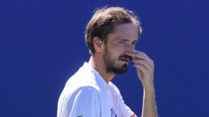Male tennis player Daniil Medvedev in white shirt touching his nose against blue background