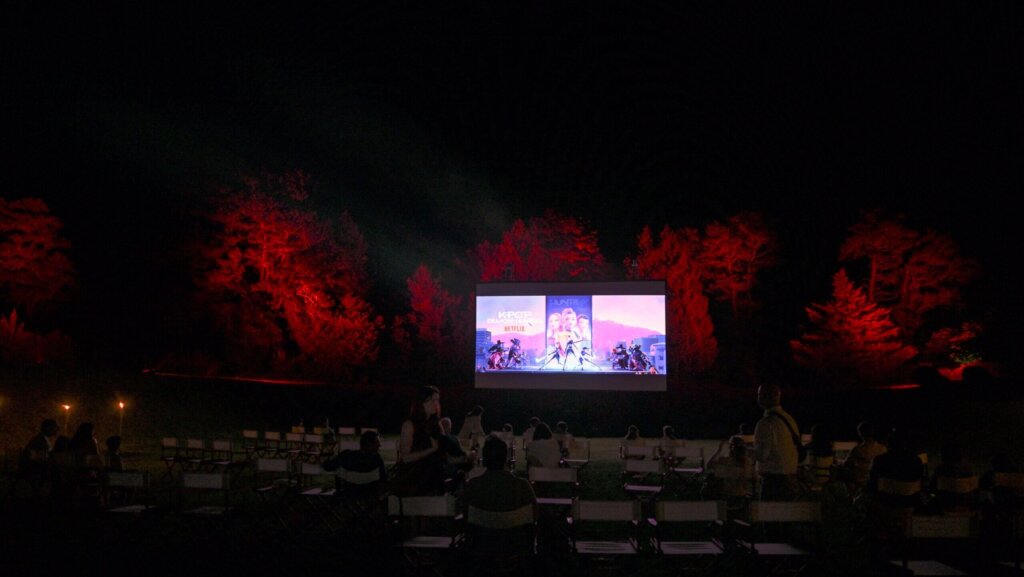 Outdoor nighttime screening of Netflix's K-Pop Demon Hunters with audience seated and red-lit trees in background
