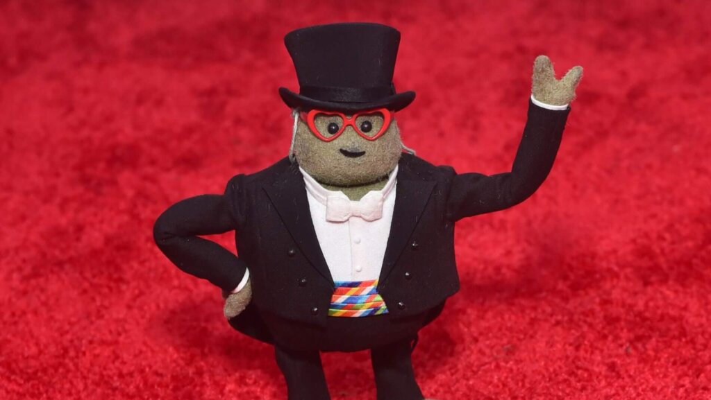 Mr. Potato Head dressed in a tuxedo, top hat, and red heart-shaped glasses on a red carpet background