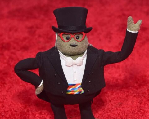 Mr. Potato Head dressed in a tuxedo, top hat, and red heart-shaped glasses on a red carpet background