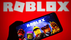 Hand holding smartphone displaying Roblox game characters with Roblox logo on red background