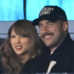 Taylor Swift and a man wearing a "Midnight Rodeo" cap smiling together indoors