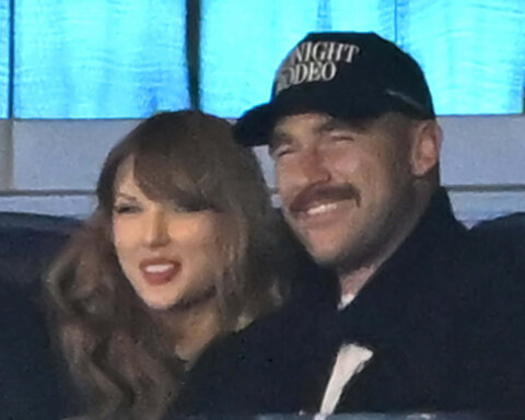 Taylor Swift and a man wearing a "Midnight Rodeo" cap smiling together indoors
