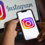 Hands holding a smartphone displaying the Instagram logo with a laptop showing the Instagram logo and text in the background