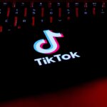 TikTok logo displayed on a smartphone screen resting on a backlit keyboard with red lighting.