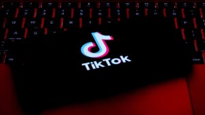 TikTok logo displayed on a smartphone screen resting on a backlit keyboard with red lighting.