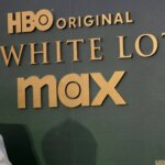 HBO Original The White Lotus Max logo on a dark green backdrop with a person in a beige suit partially visible on the left