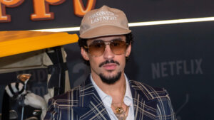 Actor and comedian Sebastian Maniscalco wearing a beige cap with "I WAS ON STAGE LAST NIGHT" text and sunglasses at a Netflix event