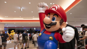 Large statue of Nintendo's Mario character with raised fist in a busy indoor event space.