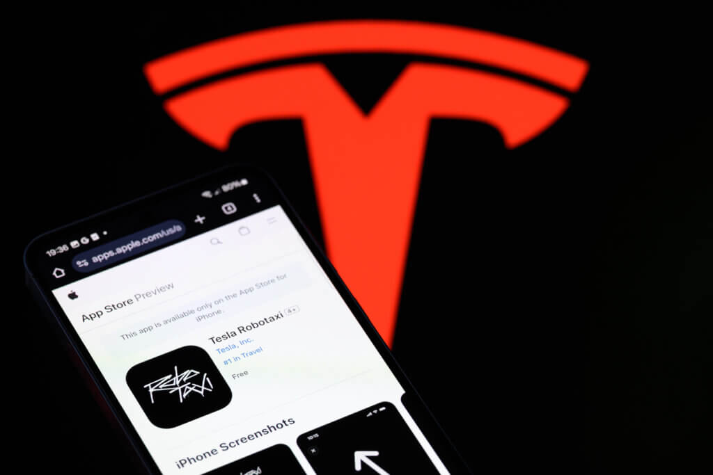 Tesla Robotaxi app page displayed on a smartphone with a large red Tesla logo in the background