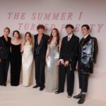 Cast members of The Summer I Turned Pretty posing at a premiere event with a branded backdrop.