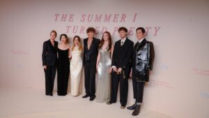 Cast members of The Summer I Turned Pretty posing at a premiere event with a branded backdrop.