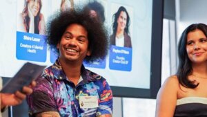 Mychal Theeist speaking at a panel with Shira Lazar and Peyton O'Hara shown on screen behind him